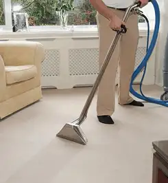 Professional carpet cleaner using a hot-water extraction wand and hose machine in a living room in Los Angeles, CA.