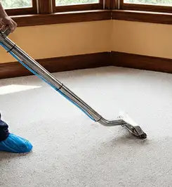 Steam carpet cleaning technician using a hot-water extraction wand on a residential carpet, wearing blue protective shoe covers Los Angeles, CA.
