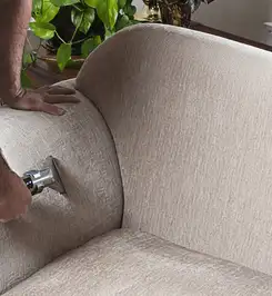 Professional upholstery cleaner deep-cleaning a fabric sofa with a handheld extraction tool and hose Los Angeles, CA.