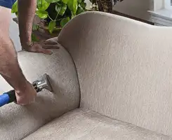 Professional upholstery cleaner deep-cleaning a fabric sofa with a handheld extraction tool and hose in Los Angeles, CA.